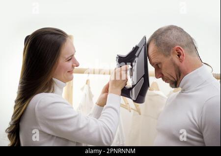 Young adult Spanish woman measuring temperature of her ill husband sitting on bed. Young beardy man getting ill, feels fatigue. Italian couple staying home because of virus. Medicine, treatment Stock Photo