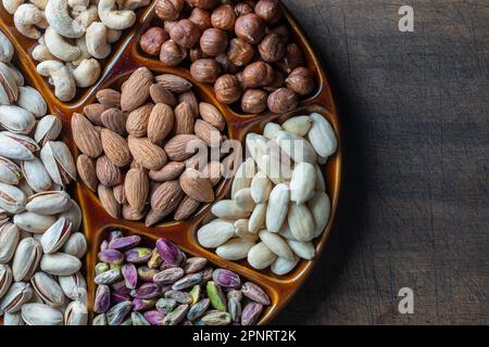 Assortment of nuts in ceramic bowl on a wooden background, close up, top view, copy space. Cashew, hazelnuts, pistachios and almonds nuts for eat. Veg Stock Photo