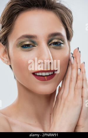 happy young woman with shimmery eye makeup and short hair standing with praying hands isolated on grey,stock image Stock Photo