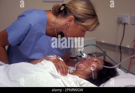 midwife consoling hispanic pregnant woman through intensive contractions with gas & air pain relief Stock Photo