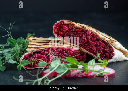 Vegan burrito. Sliced up raw food wrap with red beetroot, feta cheese, prunes, dill and cream sauce with pea microgreens on a plate. Close up Stock Photo