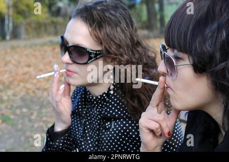 two young  women relaxing in the autumn park  and smoking cigarettes Stock Photo