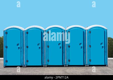 A group of outdoor portable outhouse public toilets with a blue background Stock Photo