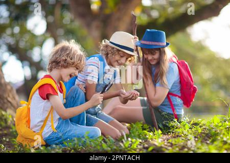 Kids explore nature. Children hike in sunny summer park. Scout club and science outdoor class. Boy and girl watch plants through magnifying glass. Stock Photo