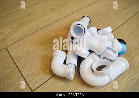 White plastic plumbing, plumbing pipes, smooth and curved, fittings, flanges, rubber gaskets. Against the background of beige boards. Stock Photo