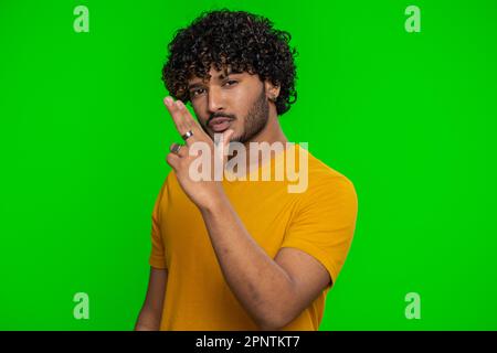 Happy young indian man pointing around with finger gun gesture, looking confident, making choice, shooting killing with hand pistol right on target. Hindu guy isolated on green chroma key background Stock Photo