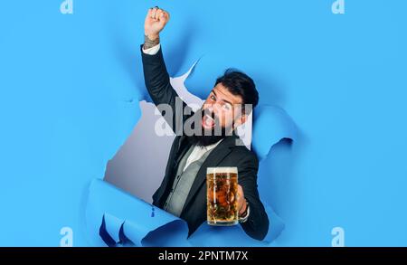 Beer time. Stylish bearded man with mug of beer raised hand. Happy man with craft beer looking through paper hole. Oktoberfest festival. Lager and Stock Photo