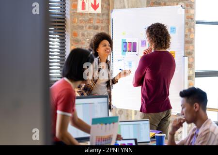 Happy diverse designers discussing project at whiteboard in busy casual office Stock Photo