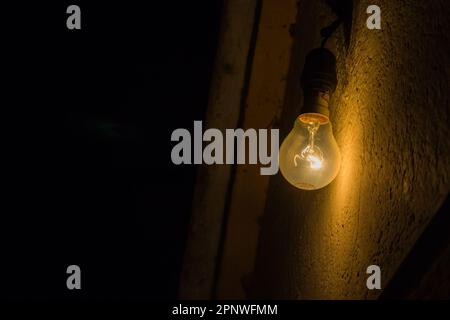 Incandescent yellow tungsten light bulb is illuminated against a wall with glowing filament with electricity. These were majorly used in household. Stock Photo