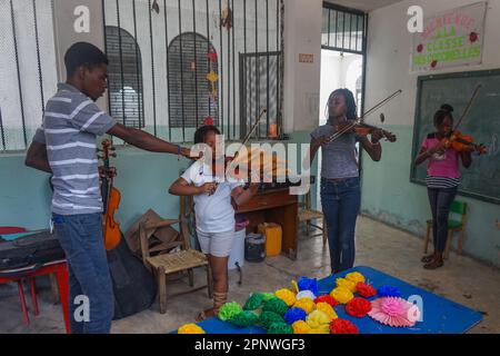 Mackenson Elsain teaches, from left, Hancia Jocelyn, 8, Rebecca Joseph, 12, and Maïrha François, 11, a violin lesson during a summer camp in Port-au-Prince, Haiti on July 21, 2022. (Anne Myriam Bolivar/Global Press Journal) Stock Photo