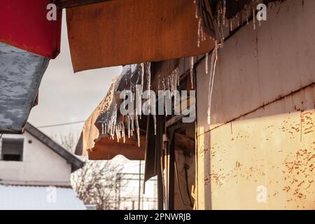 Picture of ice stalactites forming icicles on the edge of a gutter on a roof. An icicle is a spike of ice formed when water dripping or falling from a Stock Photo