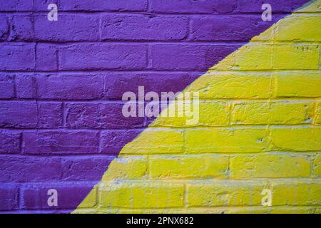 brick wall with purple and yellow spray paint Stock Photo