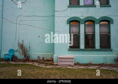 Green brick wall with windows and a plastic chair Stock Photo