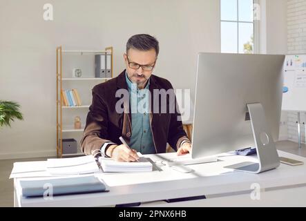 Focused middle aged man sitting at computer and filling report. Stock Photo