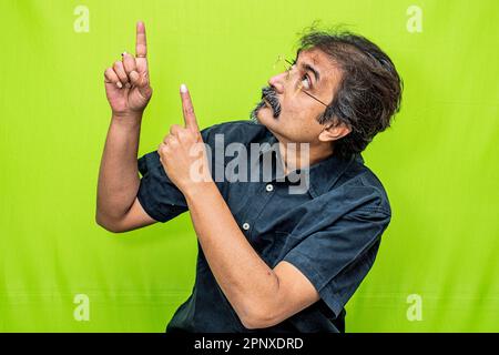 Smart corporate businessman in black shirt pointing something to the top-right with both index fingers while standing against green screen background Stock Photo