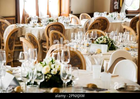 Served tables with wineglasses and white plates with cutlery and napkins prepared for wedding celebration in light restaurant Stock Photo