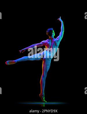 Portrait of graceful muscled male ballet dancer dancing over dark studio background with neon light. Back view. Weightless, flexible actor Stock Photo