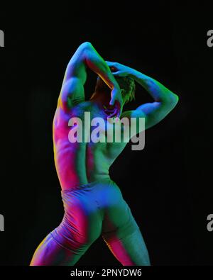 Portrait of graceful muscled male ballet dancer dancing over dark studio background with neon light. Art and beauty of male body Stock Photo