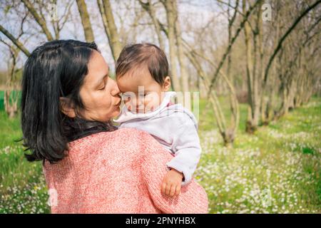 happy mother and baby daughter standing together under a tree in the countryside, smiling with love and affection. A perfect portrait of family bondin Stock Photo