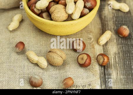 A mix of nuts in a shell, in a clay plate. A mixture of nuts on an old rustic table. Walnut, peanut, hazelnut. Food background. Place for text Stock Photo