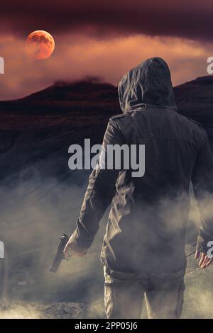 man from behind with gun in hand, background mountains and red moon Stock Photo