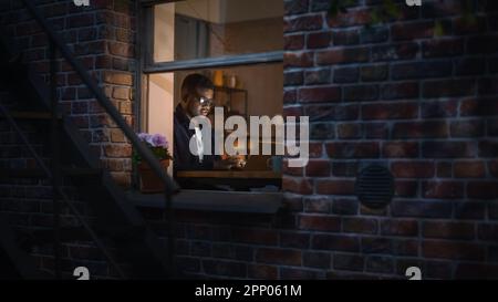 Portrait of Black Creative Young Man Working from Home on a Laptop in Cosy Warm Apartment During Night. African American Male Developer Engineering Stock Photo