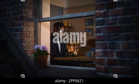 Portrait of Black Creative Young Man Working from Home on a Laptop in Cosy Warm Apartment During Night. African American Male Developer Engineering Stock Photo