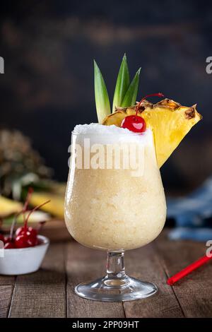 Pina colada cocktail with cherry, pineapple slice and leaves on a dark background with copy space Stock Photo
