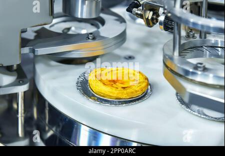 Automatic egg tart production line on conveyor belt equipment machinery in factory, industrial food production. Stock Photo