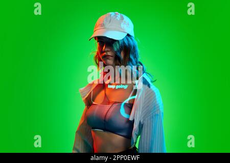 Creative portrait of young girl wearing cap with digital neon filter lights with inscryption on body on bright green mode background. Keep going Stock Photo