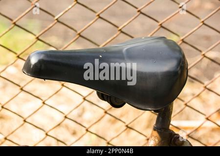 The black seat of the old bike is leaning on the side of the fence. Stock Photo
