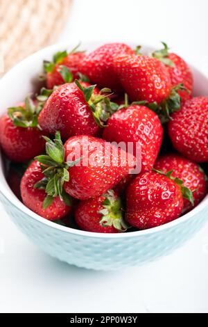 Fresh strawberries in a blue ceramic bowl, on a wicker background. Stock Photo