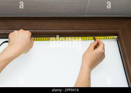 View of a man measuring a brown plastic window with a tape measure, mounting a blind on a brown plastic window Stock Photo