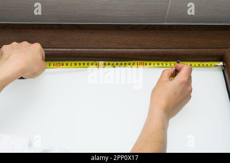 View of a man measuring a brown plastic window with a tape measure, mounting a blind on a brown plastic window Stock Photo