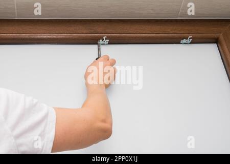 View of a man screwing a screw into a brown plastic window, mounting a blind on a brown plastic window Stock Photo