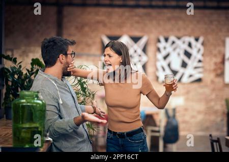 Young couple in a bar having an argument. Woman mad at man and holding his mouth shut. Stock Photo