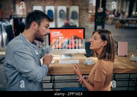 Man and woman having serious conversation at work, in front of desktop computer and work desk in a clothing shop. Business meeting, brainstorming, tea Stock Photo