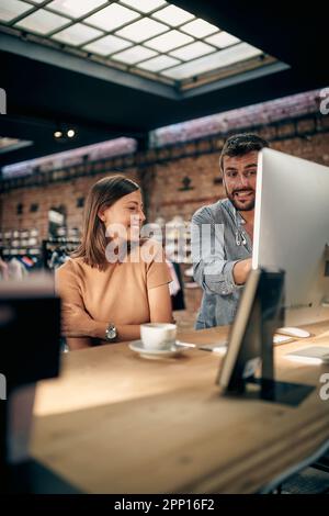 Excited young teammates working together on desktop computer. Young man and woman colleagues in clothing shop working on project together. Business, t Stock Photo