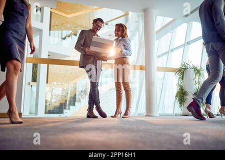 Two business colleagues are standing in a pleasant atmosphere in the hallway and watching a laptop content. Business, people, company Stock Photo