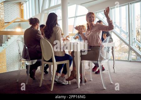 Young business people are sitting around the table during a lunch break in a friendly atmosphere in the company building and having a good time while Stock Photo
