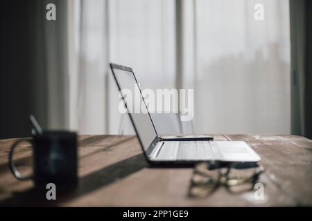 Laptop on a wooden table, a cup of coffee, glasses and a mobile, in a warm and comfortable light environment Stock Photo