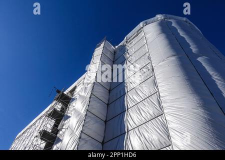 House building, construction, restoration or maintenance site with scaffolding and protective covering of gray tarpaulin Stock Photo