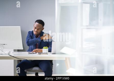 Young Businessman Having Shoulder Pain While Working At Computer Desk In Office Stock Photo
