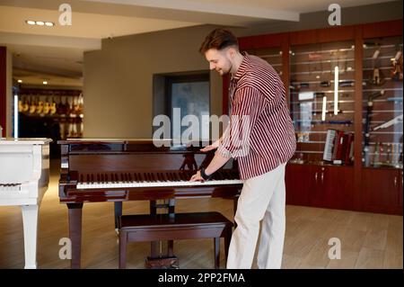 Young stylish handsome man playing piano at musical shop Stock Photo