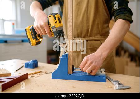 Man carpenter making holes in wooden plank using electric instrument Stock Photo