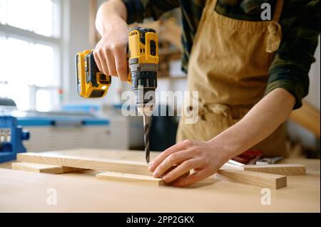 Carpenter working with drill leaning over table at carpentry workshop Stock Photo