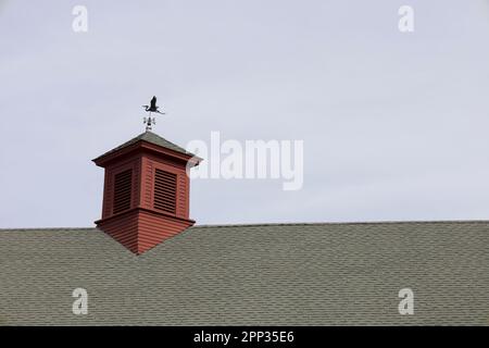 Roof top of red barn with weathervane on top of tower.  Taken on a cloudy day in Concord, Massachusetts, USA. Stock Photo