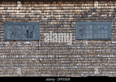 Old Rhode Island barn with wooden shingles and two window with green painted trim. Stock Photo