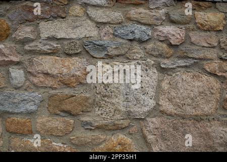 Rock wall with sandy and gray tones.  Natural lighting on the building's wall.  Stones are of various shapes and colors. Stock Photo