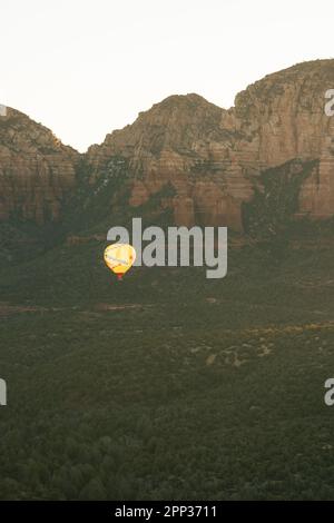 Vertical image of wide shot of yellow hot air balloon releasing flames to gain altitude in early morning flight. Stock Photo